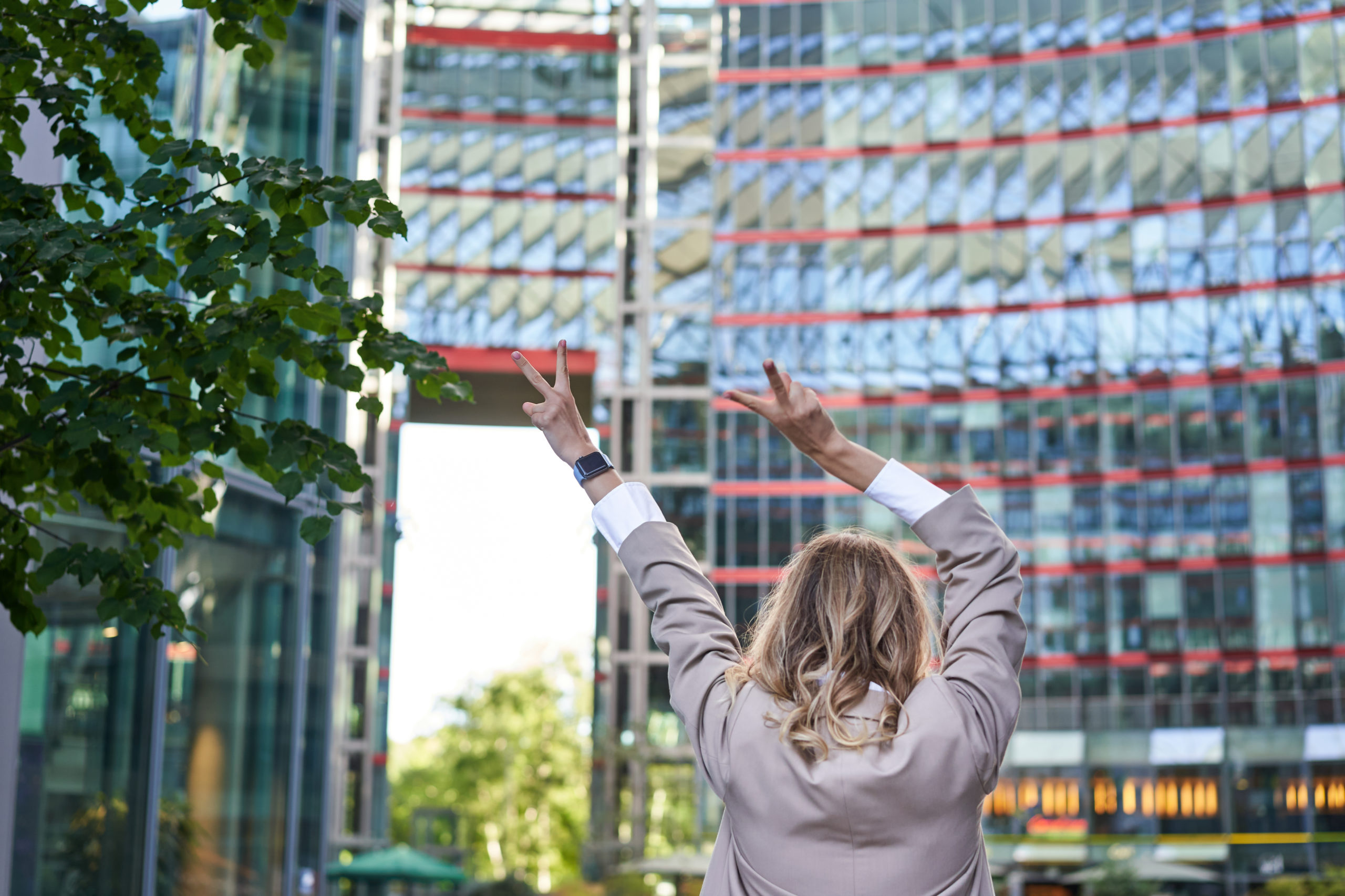 Corporate people. Rear view of businesswoman raising hands up in celebration, triumphing, achieve goal and rejoicing, standing on street